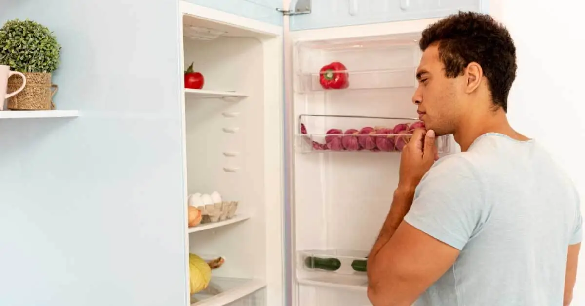 A person standing infront of a refrigerator that is not cooling. He is thinking about the issue why his refrigerator is not cooling